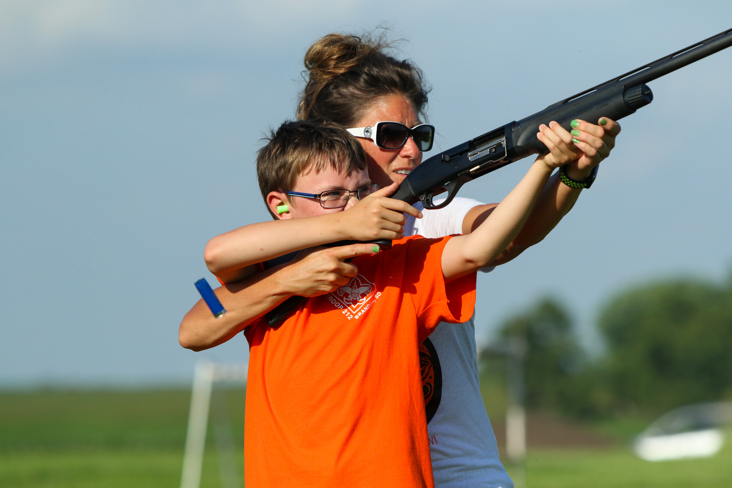 female shooting instructor helping a youth shoot a shotgun