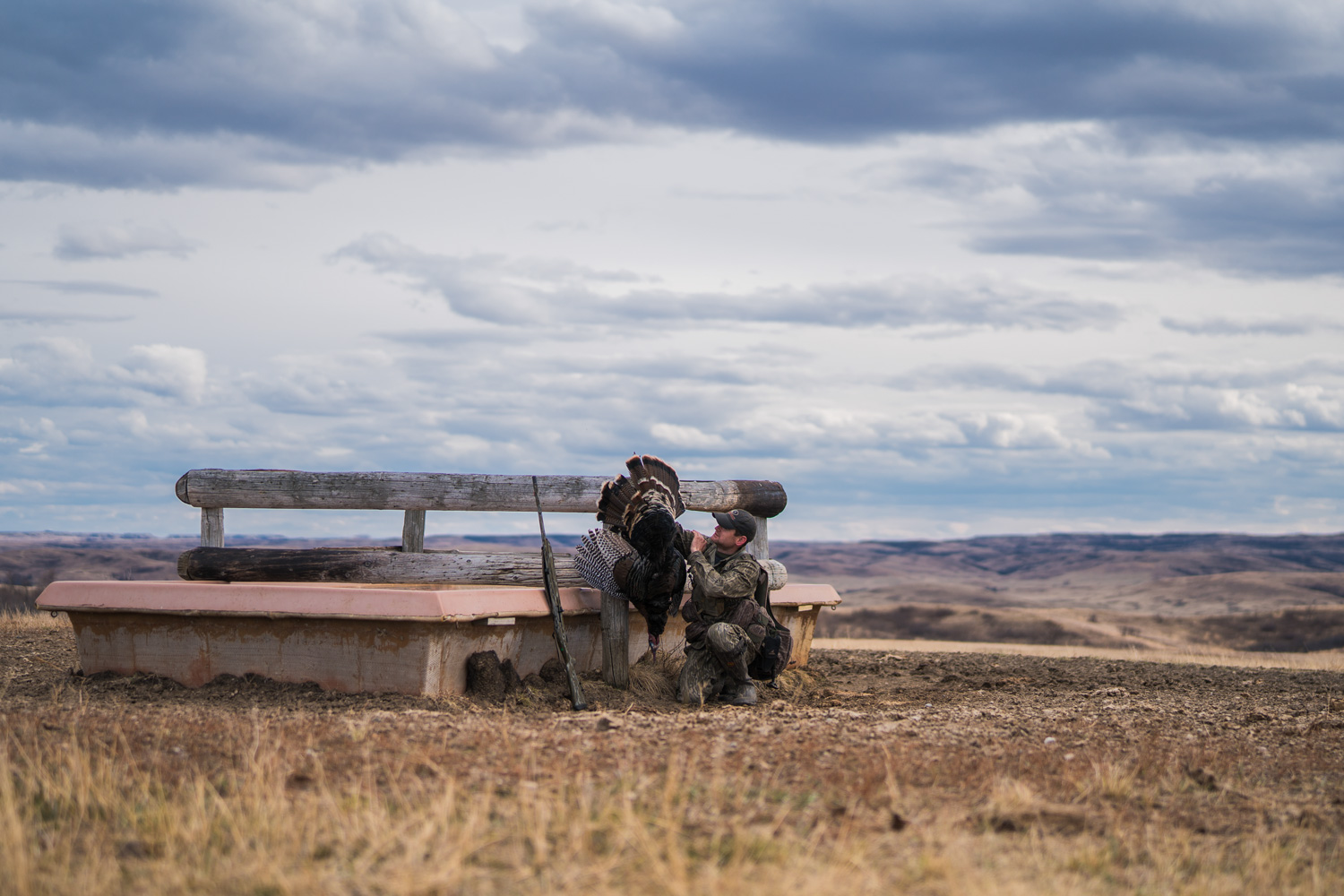 hunter posing with a turkey at a watering hole on the open plains