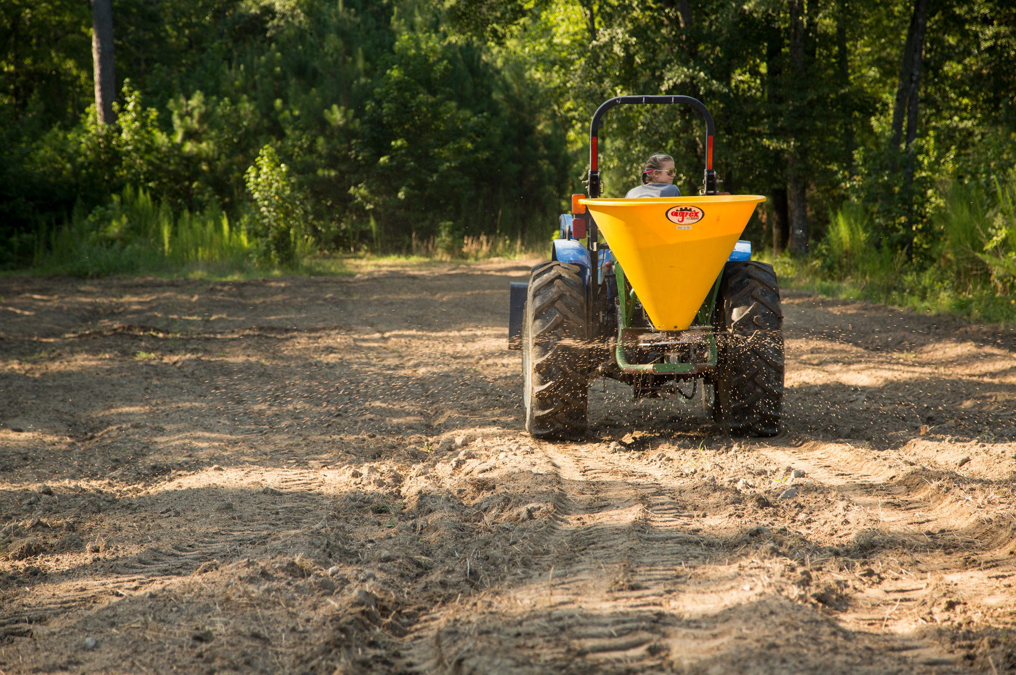 female running a tractor with a seed spreader through a food plot