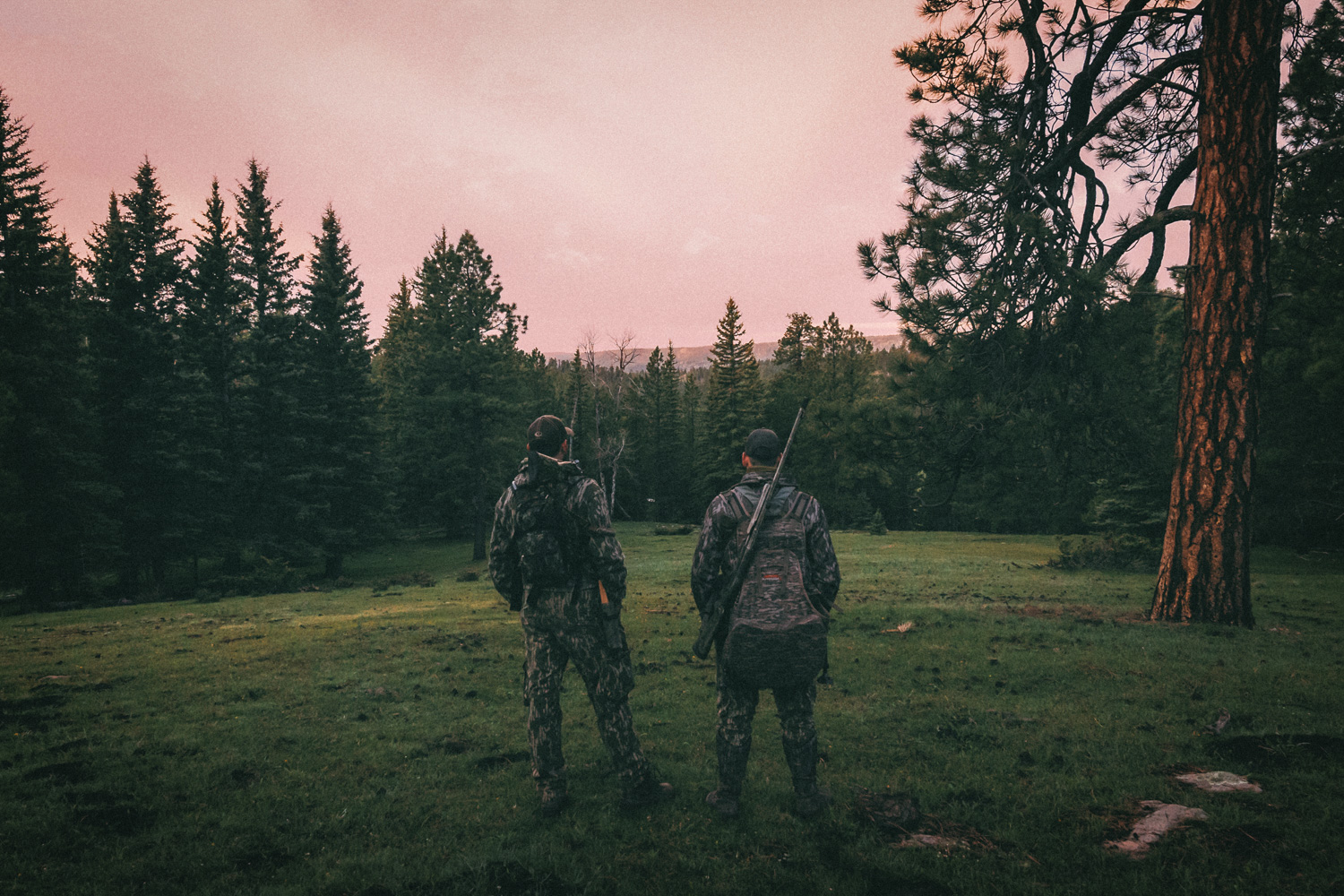 two hunters on the edge of a meadow in the mountains