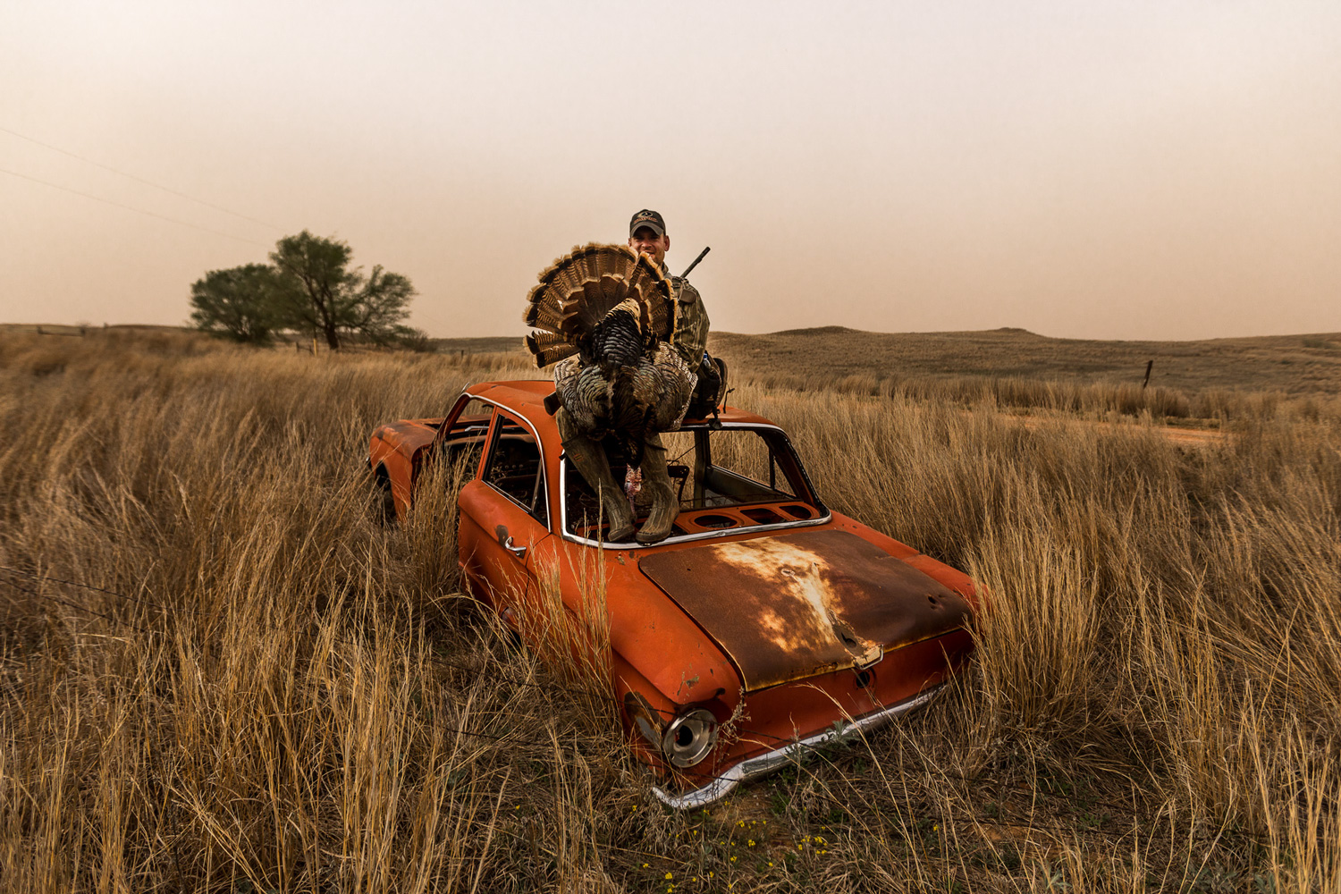 hunter with harvested turkey posing on a car in the plains