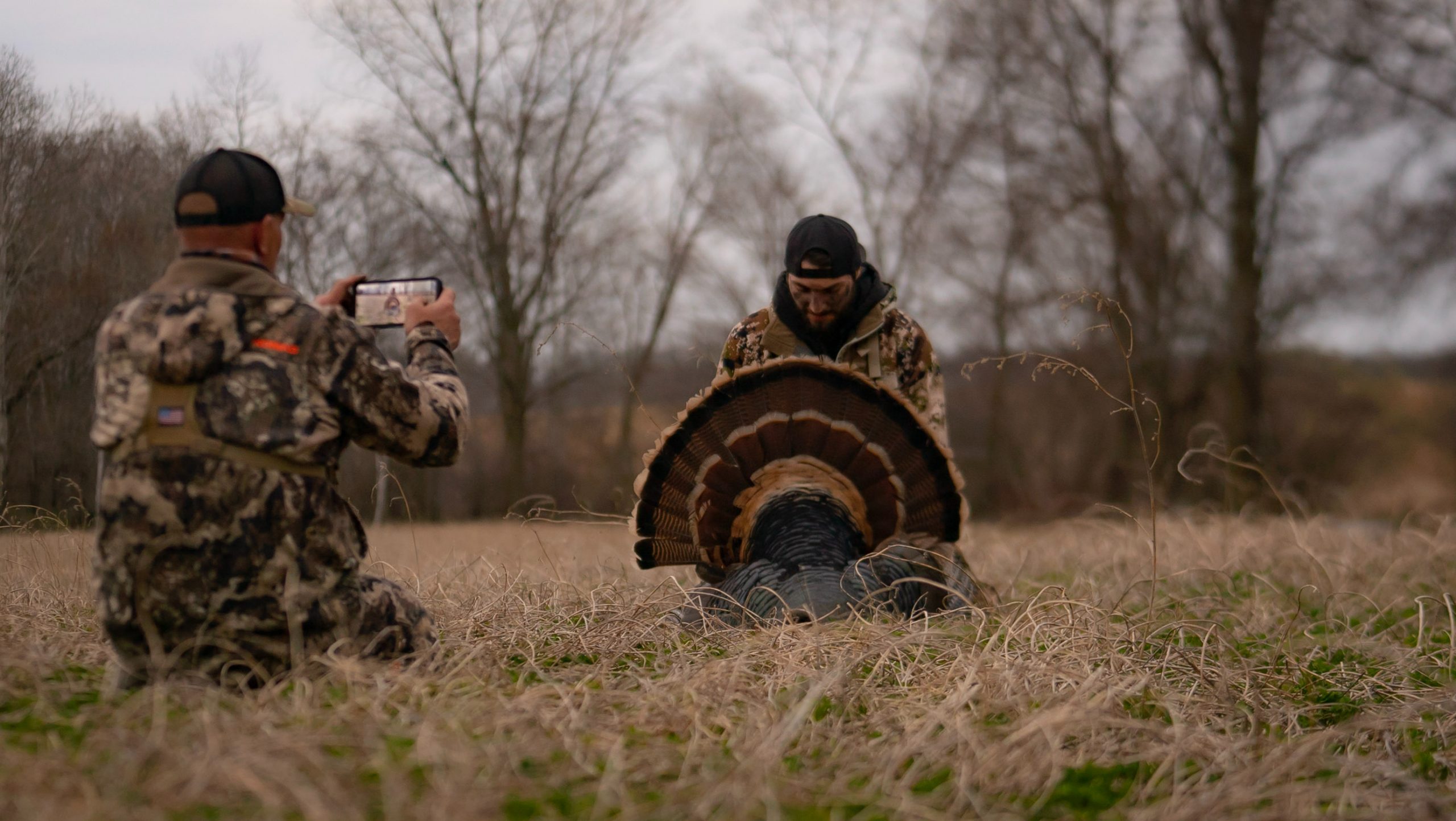 hunter takes a photo of another hunter with his harvested turkey