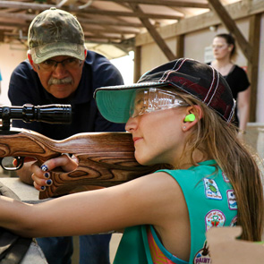 girl shooting an air rifle with a shooting instructor watching